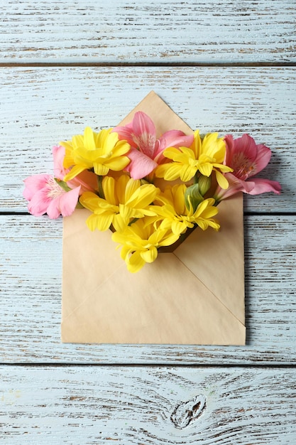 Alstroemeria rosa e crisântemo amarelo em envelope em fundo de madeira