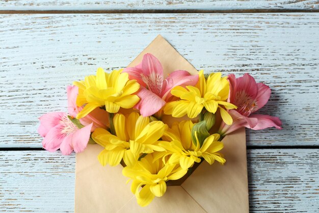 Alstroemeria rosa e crisântemo amarelo em envelope em fundo de madeira