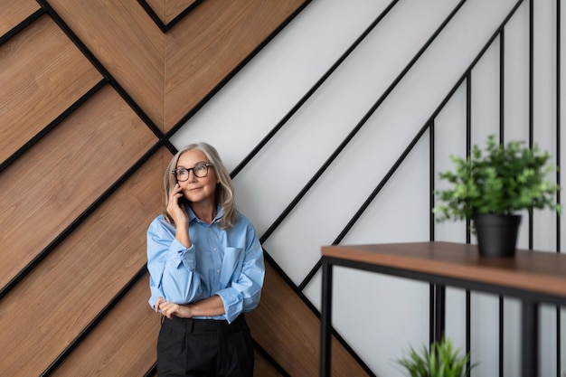 Foto la alta directora adulta habla por teléfono móvil en el contexto de un profesional de oficina moderno