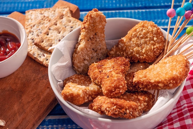 Alta vista de algunas nuggets de pollo frito en un tazón blanco acompañado de ketchup con algunas galletas