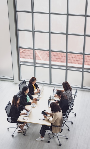 Alta vista de seis empresárias executivos sentados em cada cadeira, usando laptops e tablets na mesa de conferência de madeira na sala de reuniões no escritório. Conceito para reunião de negócios.