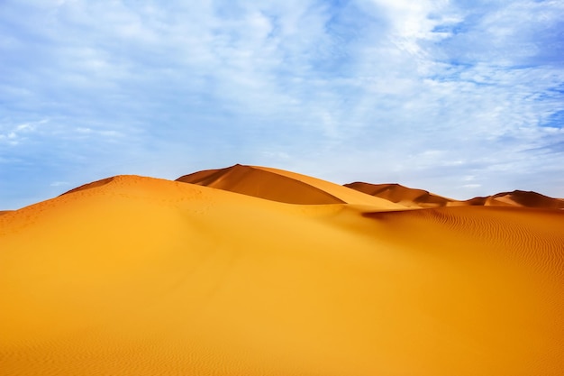 Altas dunas de arena del desierto del Sáhara contra un cielo azul con nubes