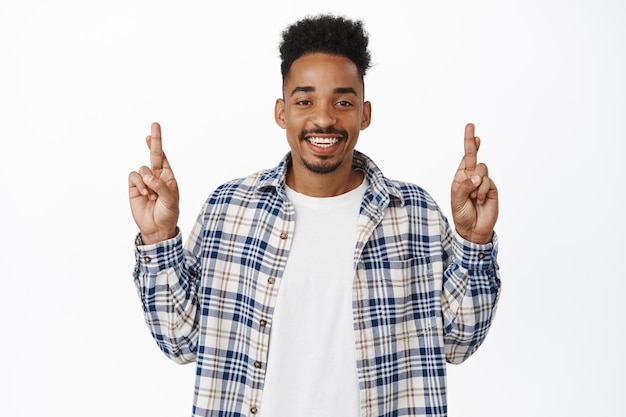 Altas esperanças. Sorrindo feliz jovem afro-americano cruza os dedos para dar sorte, fazendo um desejo esperançoso, esperando por notícias positivas, antecipando prazer, fundo branco