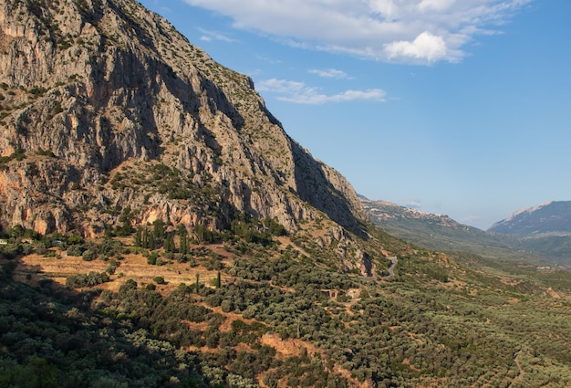 Altas montañas, valle verde, olivos y camino de montaña. En el fondo está el cielo azul