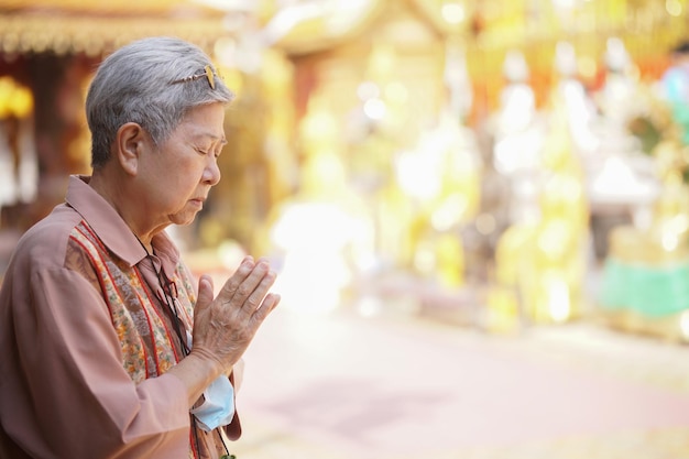 Alte asiatische ältere Seniorin reisende Touristin, die im buddhistischen Tempel betet.