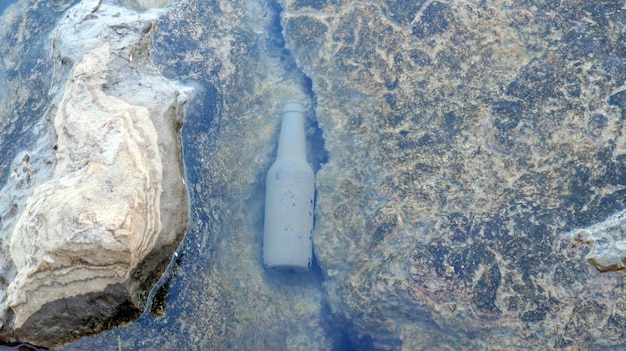 Alte Flasche im Meer auf Felsen, Algenplakette auf der Flasche, Umweltverschmutzung, Müll im Meer