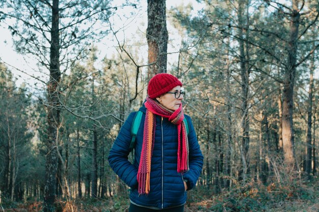 Alte Frau auf Winterkleidung und Hut, die während eines Tages im Freien lächelt Seniorenaktivitäten in der Natur während des Sonnenuntergangs Konzept der Großmutter für psychische Gesundheit