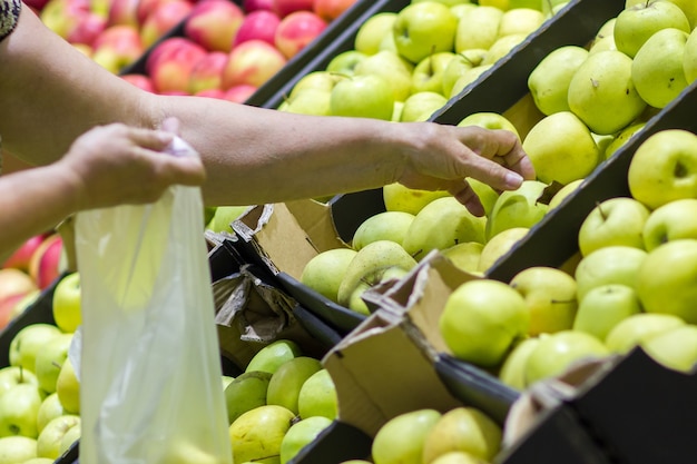 Alte Frau, die frische Äpfel in der Lebensmittelabteilung auswählt und in Plastiktüte steckt.