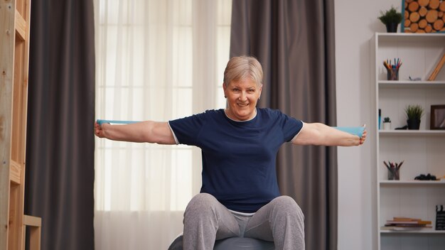 Alte Frau, die körperliches Training auf Fitnessball sitzt. Alte Frau, die Training gesunder Lebensstil Sport-Fitness-Training zu Hause mit Hantel-Aktivität mit Gewichten hebt