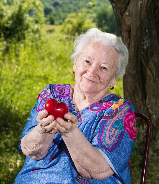 Alte Frau, die rotes Herz in den Händen draußen hält