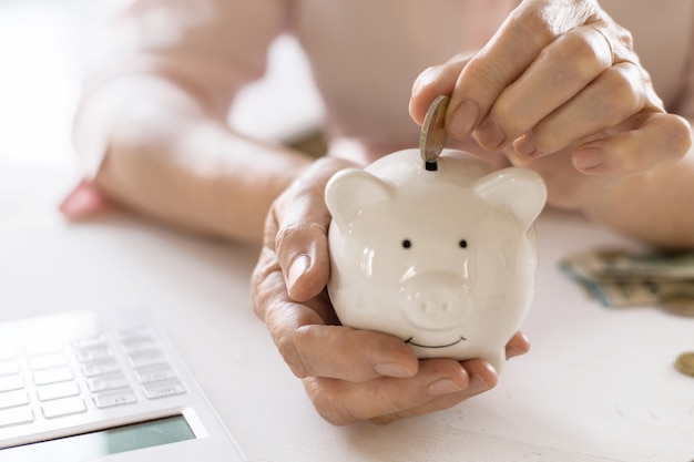 Foto alte frauenhände stecken geld in das sparschwein, das konzept von ruhestand, sparen.