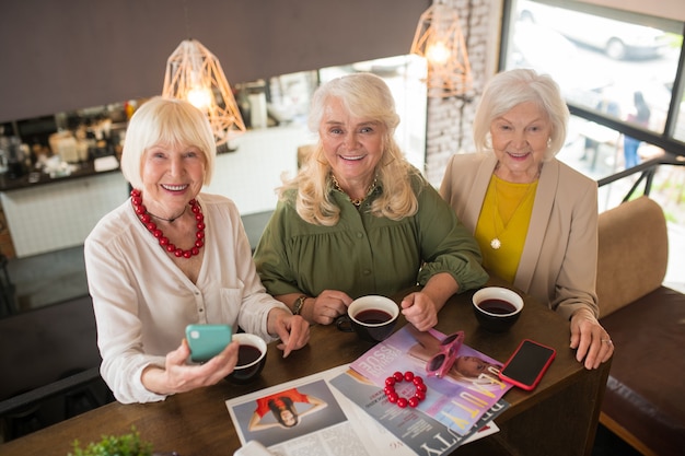 Alte Freunde. Frauen sehen fröhlich aus, während sie zusammen am Tisch sitzen