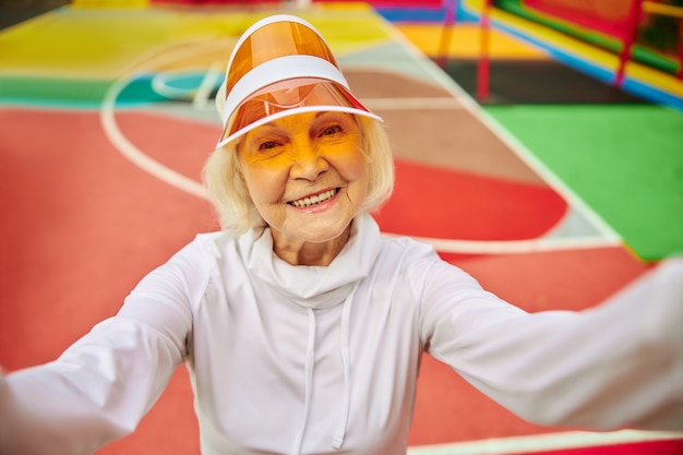 Alte, gesunde und fröhliche Dame auf einem bunten Platz im Freien