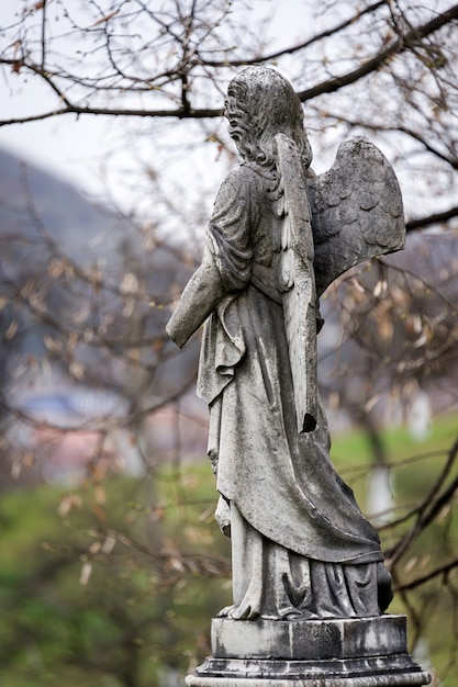 Alte Grabsteinskulptur eines Engels mit gebrochenem Arm und Flügeln auf dem Friedhof