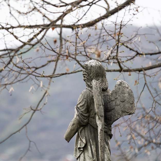 Alte Grabsteinskulptur eines Engels mit gebrochenem Arm und Flügeln auf dem Friedhof