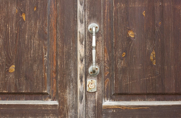 Alte hölzerne Eingangstür mit Metallgriff. Eine heruntergekommene antike Tür mit eisernem Griff