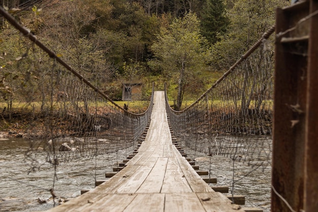 Alte hölzerne Hängebrücke über Bergfluss zwischen herbstlichen Wald stimmungsvolles Bild Landschaftshinter...