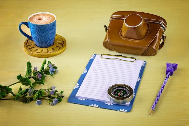 Alte kamerablaue Notizbuchtasse Cappuccino-Kompass exotische Blume auf gelbem Hintergrund