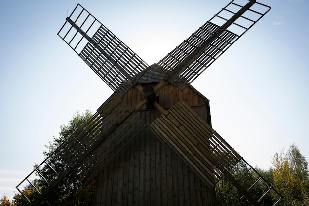 Alte Mühle auf einem Hintergrund von blauem Himmel und Bäumen. Windmühle an einem bewölkten Tag. Foto in hoher Qualität