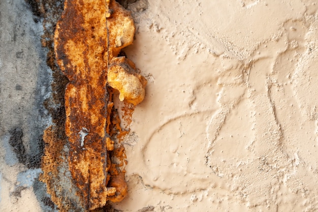 Alte raue beige gestrichene Wand mit Rissen und Löchern, bedeckt mit rostigem Sprühschaum