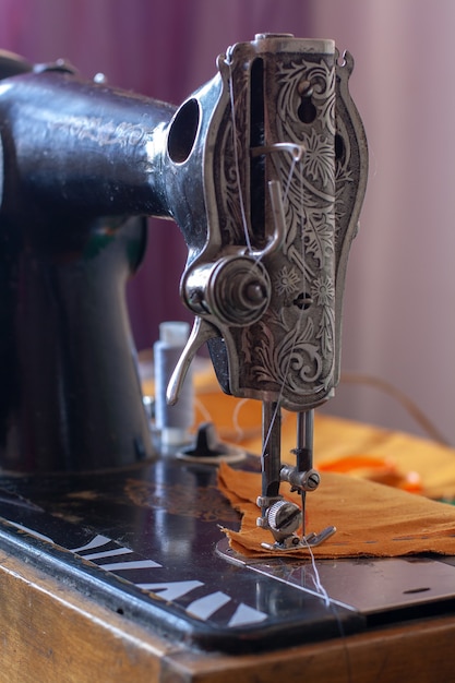 Foto alte retro-nähmaschine und orangefarbener stoff zum nähen bereit. der nähfuß wird abgesenkt. geringe schärfentiefe. konzentrieren sie sich auf den nähfuß. vertikal.