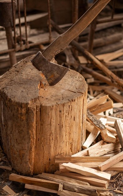 Alte rostige Axt mit Holzgriff, die im Stumpf stecken, verschwommener Hintergrund mit Haufen von Holzstämmen Große Axt ragt in gefälltem Holz im Hintergrund des Waldes hervor Verschwommener Hintergrund Konzeptwerkzeugarbeit