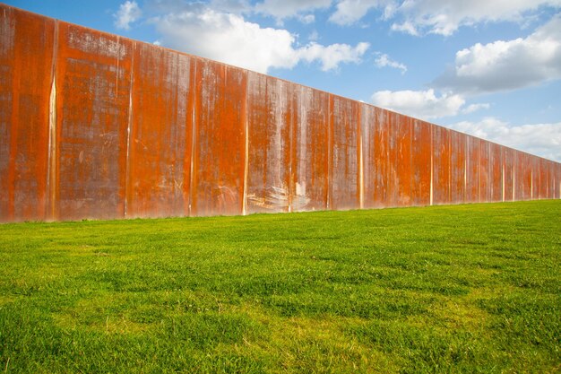 Alte rostige Metallzaunwand auf grüner Wiese mit blauem Himmel im Hintergrund