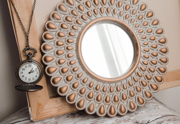 alte runde Vintage-Uhr an einer Kette neben einem runden Spiegel im Innenraum