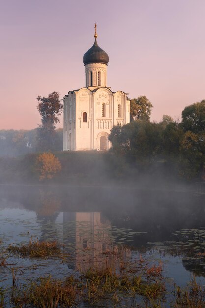 Alte russisch-orthodoxe Kirche, die von der aufgehenden Sonne beleuchtet wird, spiegelt sich im Teich unter den Herbstbäumen Vladimir Russia