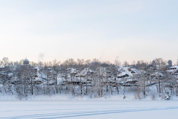 Alte russische Dorfhäuser mit Schnee bedeckt auf einem Hügel in der Nähe des zugefrorenen Sees