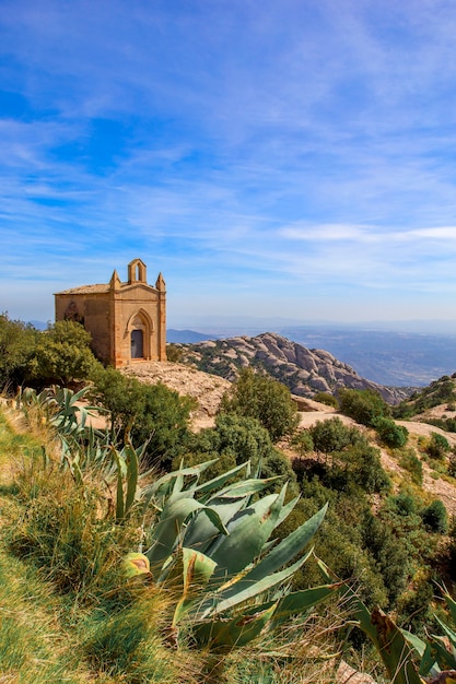 Alte Steinkirche oben auf Hügel am sonnigen Sommertag. Montserrat Berge in Spanien. Vertikales Foto.