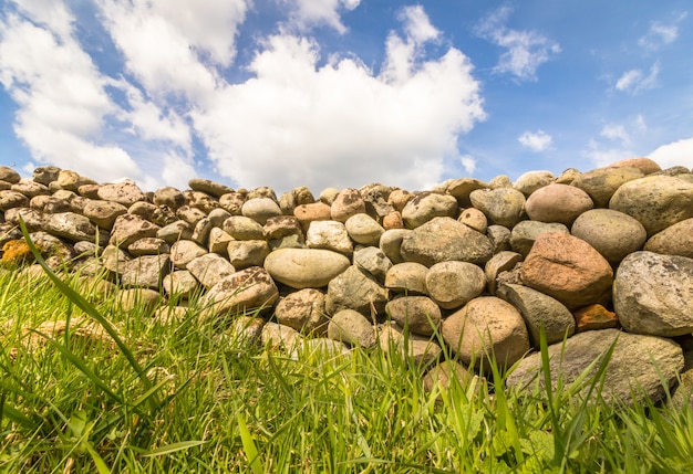Alte Steinmauer mit grünem Gras vorne und blauem Himmel mit Wolken oben