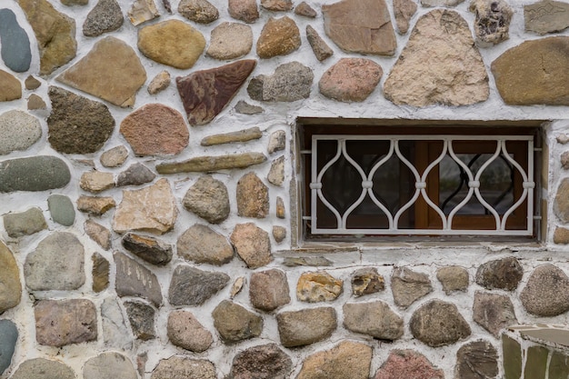 Alte Steinmauer und weißes Gitter auf einem Fenster.