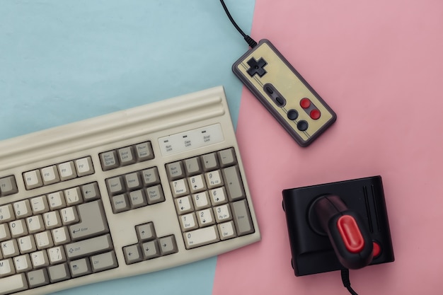 Alte Tastatur, Joystick und Gamepad auf blauem rosa Hintergrund. Retro-Gaming. 80er Jahre. Ansicht von oben. Flach legen