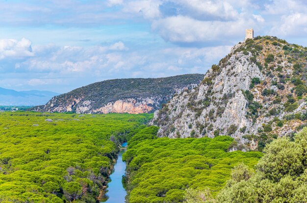 Alte Turmruinen im Naturschutzgebiet der Maremma, Toskana, Italien. Ausgedehnter blauer Fluss des Kiefernwaldes im grünen Wald im Naturpark, dramatische felsige Landzunge der Küste