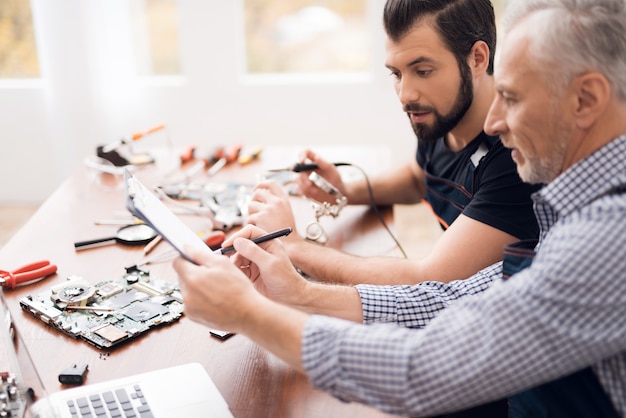 Alte und junge Ingenieure reparieren defektes Motherboard.