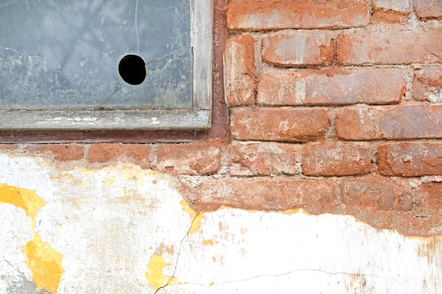 Alte Ziegelmauer mit einem Fragment des zerbrochenen Fensters und mit altem Gips