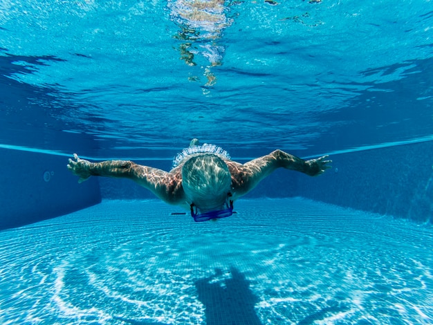 Alter älterer Mann des aktiven Menschen, der unter Wasser auf einem blauen Poolwasser mit Tauchmaske schwimmt