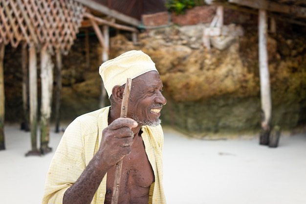 Alter afrikanischer Hirte, der am Strand mit Stock spazieren geht