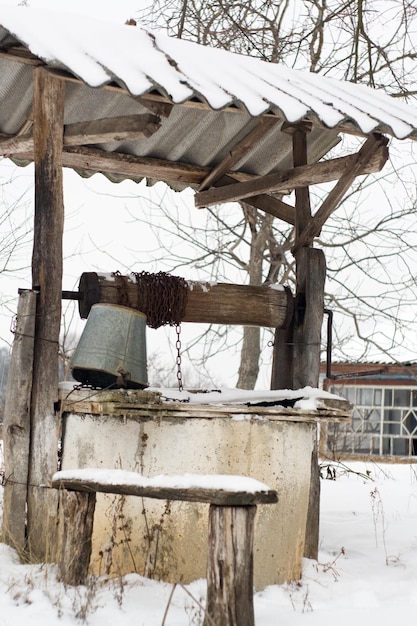 Alter Brunnen mit einem Eimer in der Nähe des Hauses am Wintertag