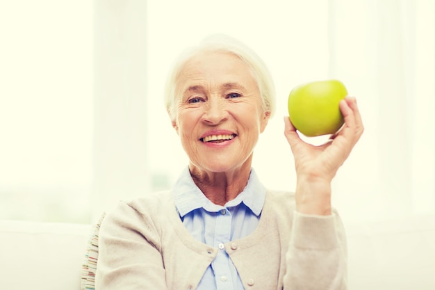 alter, gesunde ernährung, lebensmittel, ernährung und personenkonzept - glücklich lächelnde seniorin mit grünem apfel zu hause