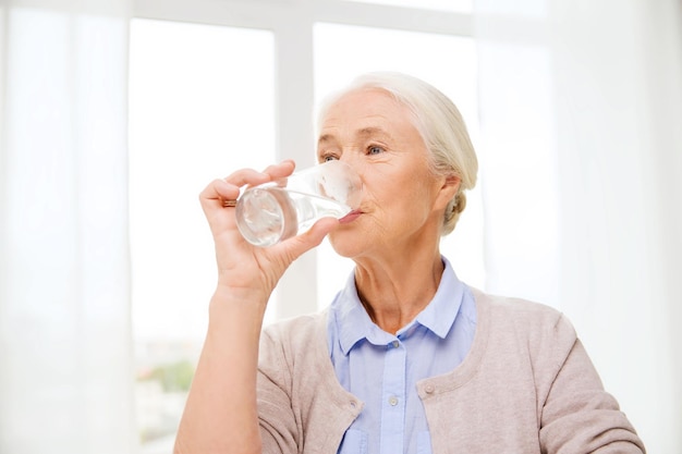 alter, gesundheitswesen und personenkonzept - glückliche seniorin mit glas wasser zu hause