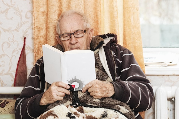 Alter Großvater auf dem Sofa mit einem Buch in seinen Händen Freizeit für ältere Menschen