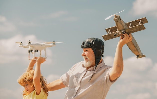 Alter Großvater und kleiner Enkel mit Flugzeug und Quadrocopter-Drohne über blauem Himmel und Wolken ba