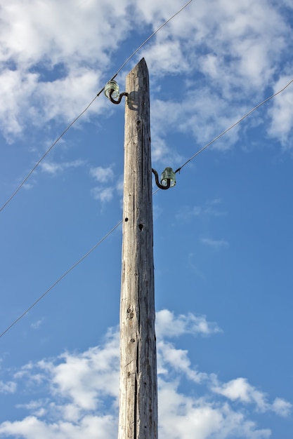 Alter hölzerner elektrischer Pol gegen den blauen Himmel und die Wolken