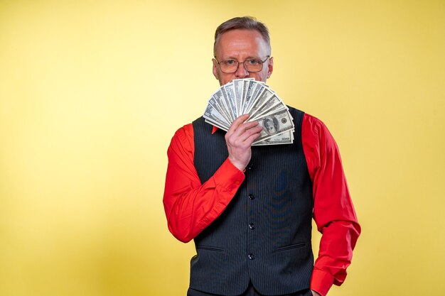 Alter lächelnder grauhaariger Mann mit Brille. Mann, der Dollar-Fan in der Nähe von Gesicht hält. Menschliche Emotionen und Mimik