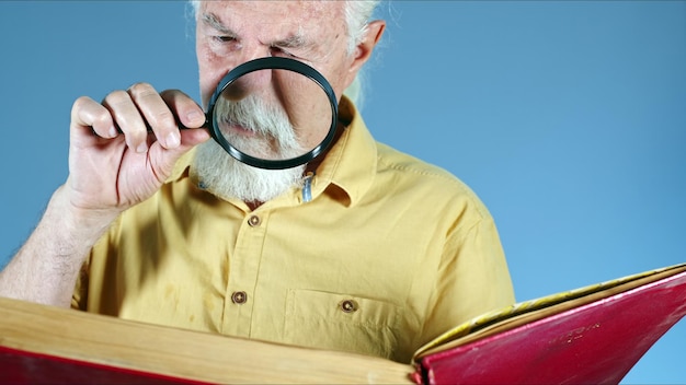 Alter Mann, der Buch mit Vergrößerungsglas-Foto betrachtet