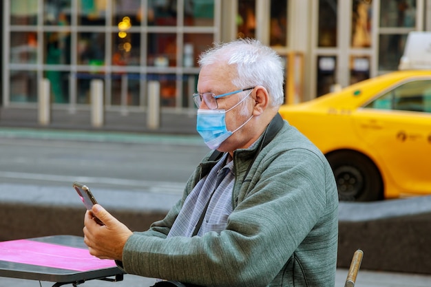 Alter Mann, der sein Handy benutzt, während er die Straßenmaske entlang geht, um sich während der Pandemie in New York vor dem Coronavirus zu schützen