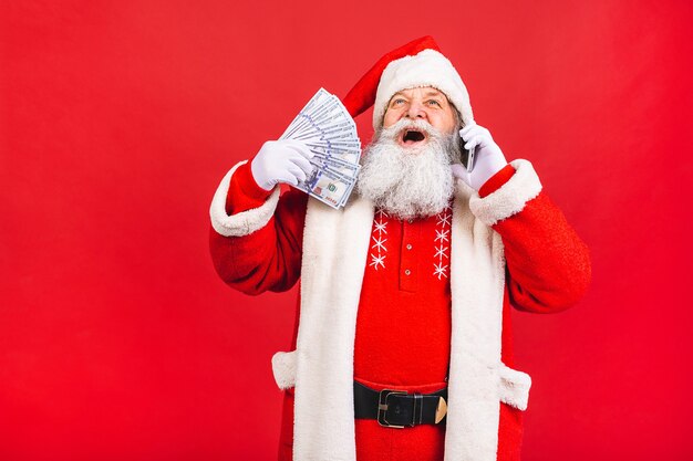 alter Mann im Weihnachtsmannkostüm, das auf einem Mobiltelefon lokalisiert auf rotem Hintergrund spricht