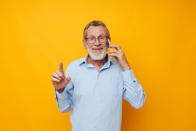 Alter Mann in blauem Hemd und Brille, der am Telefon spricht, gelber Hintergrund